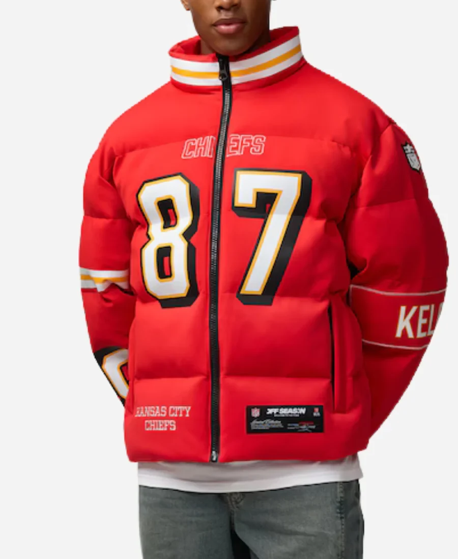Front view of a man wearing the red Travis Kelce Chiefs off season puffer jacket featuring #87 chest graphic, central zipper, and striped collar. Travis Kelce Chiefs Off Season Puffer Jacket